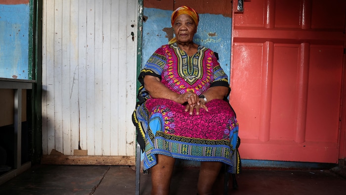 Ouma Katrina Esau, en tenue sud-africaine, assise sur une chaise.