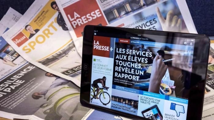 L'application La Presse+ est ouverte sur une tablette électronique, devant des cahiers de l'édition papier de La Presse.