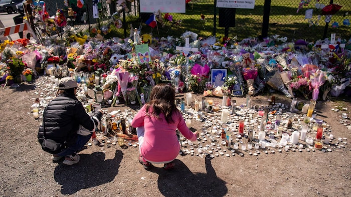 Les personnes devant des photos et fleurs déposées en hommage aux victimes.
