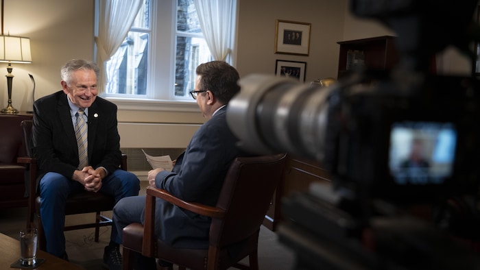 Larry Smith en entrevue avec un journaliste devant une caméra dans un bureau.