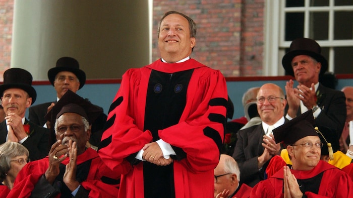 Larry Summers se tient debout à l'avant de personnes assises qui applaudissent.