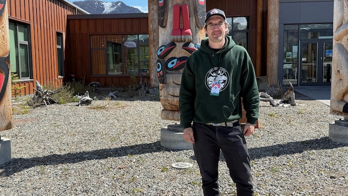 Lars Jessup debout devant des totems et regarde vers l'appareil photo.