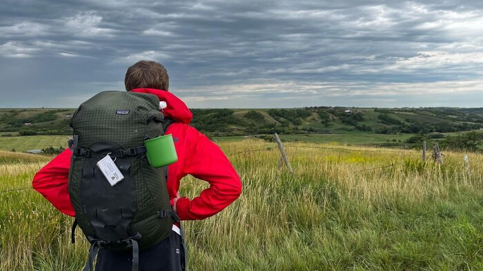 Un homme en tenue de randonnée admire le paysage verdoyant devant lui.