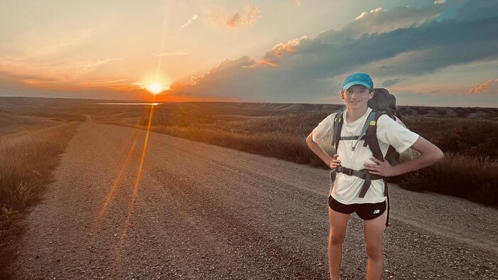 Un jeune homme est debout sur une route en gravier de la Saskatchewan et pose devant un coucher de soleil.