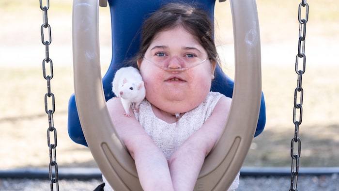 Un rat blanc sur l'épaule gauche de Lauralie. La petite est dans une balançoire adaptée pour enfants handicapés.