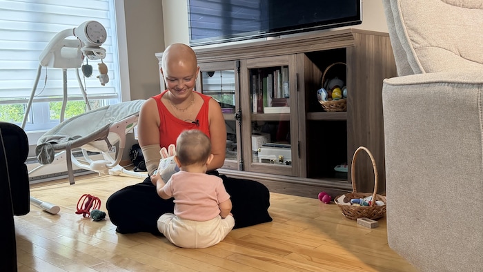 Laurélie est assise sur le plancher et joue avec sa fille de huit mois.