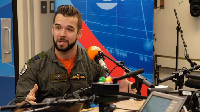 Un homme savamment coiffé, en uniforme de l'aviation canadienne, est assis dans un studio de radio.