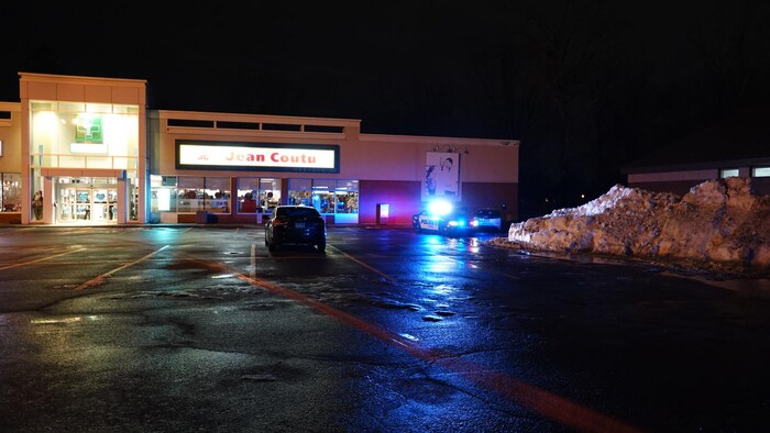 Une voiture de police est stationnée devant une pharmacie avec les gyrophares allumés.