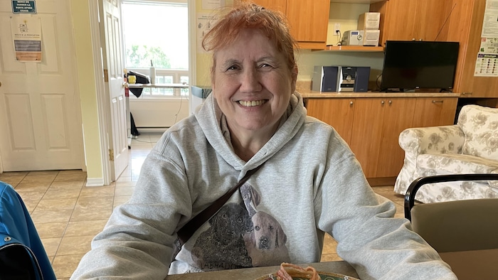 Claire participe aux activités de l'organisme communautaire de soutien en santé mentale L'Avant-garde, situé en Montérégie. Souriante, elle est assise dans la cuisine de cet organisme.