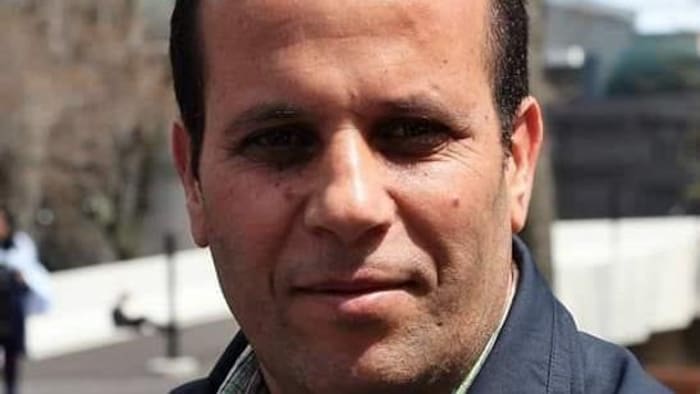 Lazhar Zouaïmia, cheveux bruns, sourire en coin, chemise quadrillée.
