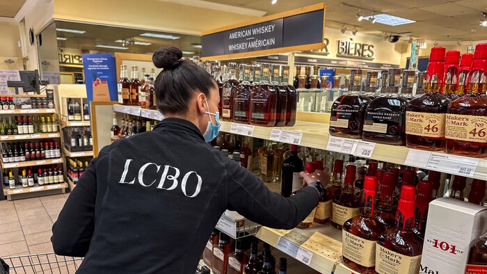 Une employée place des bouteilles de whiskey américain sur des tablettes dans une succursale de la LCBO.