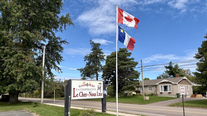 Il est écrit sur un panneau "La Coopérative Le Chez-Nous" juste à côté de drapeaux acadien et canadien sur la rue principale de Wellington. 