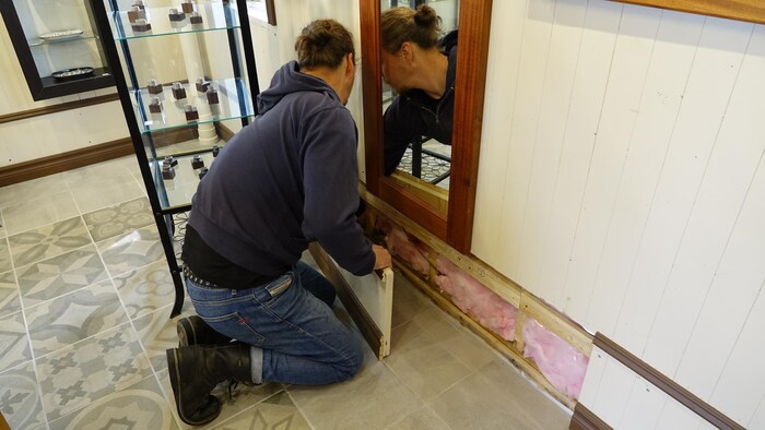 Un homme enlève le bas des murs pour montrer l'isolant.