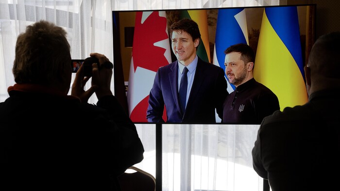 Des journalistes filment un écran de télévision pendant que le président ukrainien Volodymyr Zelensky salue le premier ministre canadien Justin Trudeau à Kiev, en Ukraine, le lundi 24 février 2025.