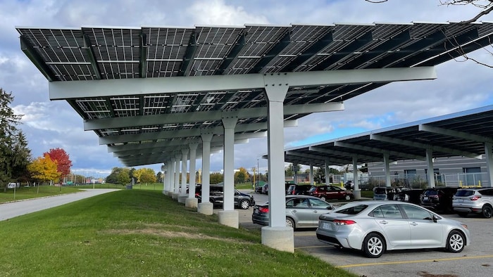 Des véhicules sont stationnés sous des panneaux solaires.