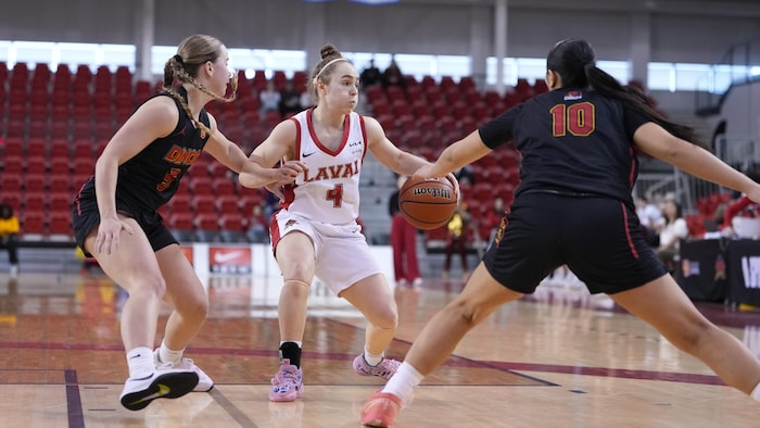 Une joueuse du Rouge et Or dribble avec le ballon avec deux joueuses des Dinos autour d'elle. 