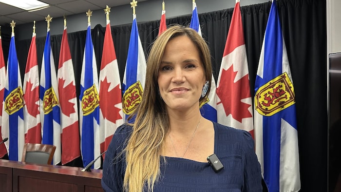 Leah Martin pose pour la photo devant une rangée de drapeaux de la Nouvelle-Écosse et du Canada.