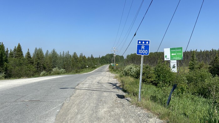 L'entrée en asphalte d'un chemin forestier identifié R1000 sur un petit panneau indicateur.