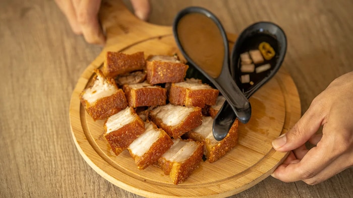 Lechon kawali na nasa kahoy na serving plate na may kasamang sarsa at sawsawan.