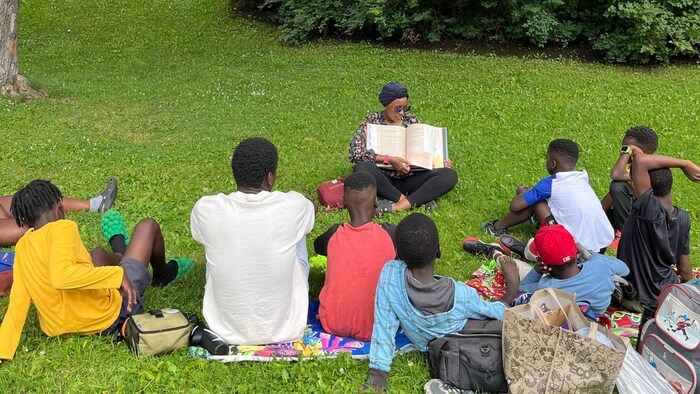 Un adulte lit un livre à des enfants assis dans un parc.