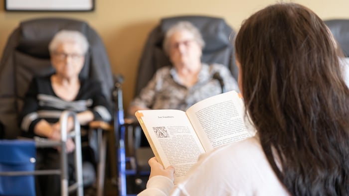 Une femme lit un livre à deux aînées devant elle.