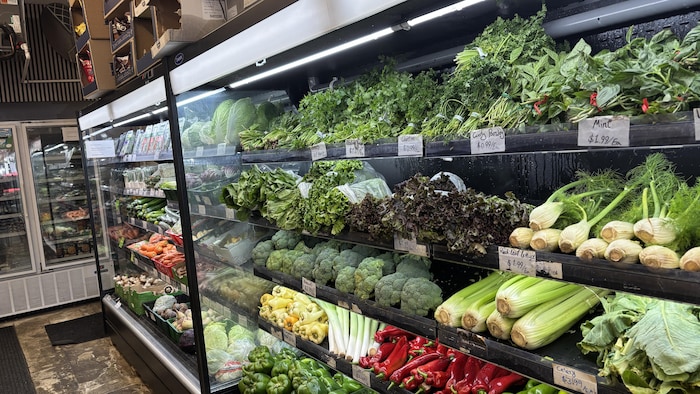 Des légumes verts comme des laitues, des céleris, et des poivrons, sur des étagères d'épicerie.