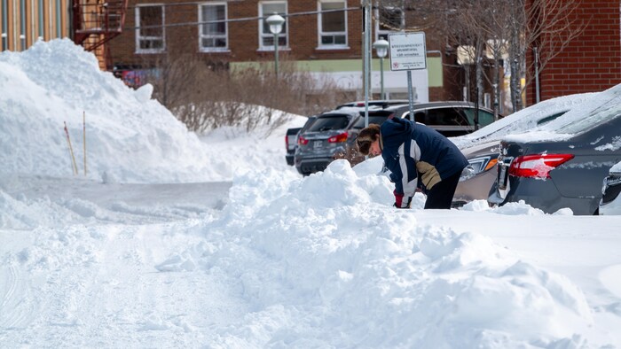 Une personne pelte sa voiture hors d'un banc de neige.