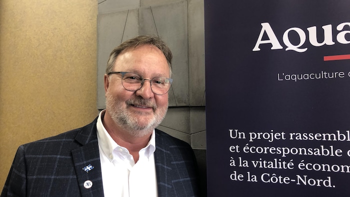 Un homme sourit à côté d'une affiche.