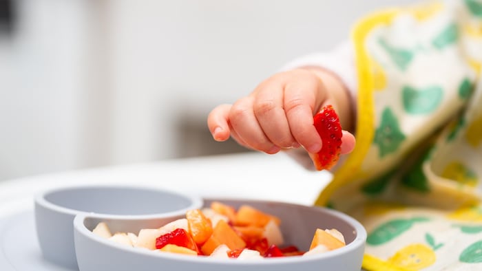 Un bébé prend une fraise dans sa main.