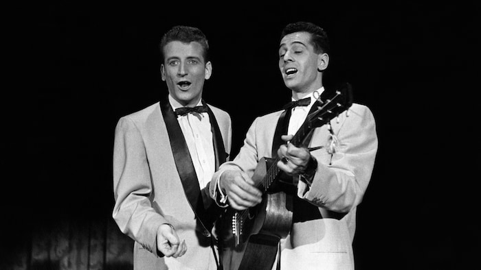 Dans un studio de télévision, les deux hommes chantent, l'un d'eux s'accompagnant à la guitare.