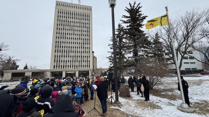 Des gens rassemblés à l'extérieur face au drapeau fransaskois.
