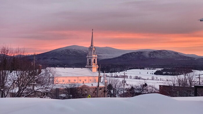 Les rayons du soleil reflètent sur une église dans un paysage hivernal. 