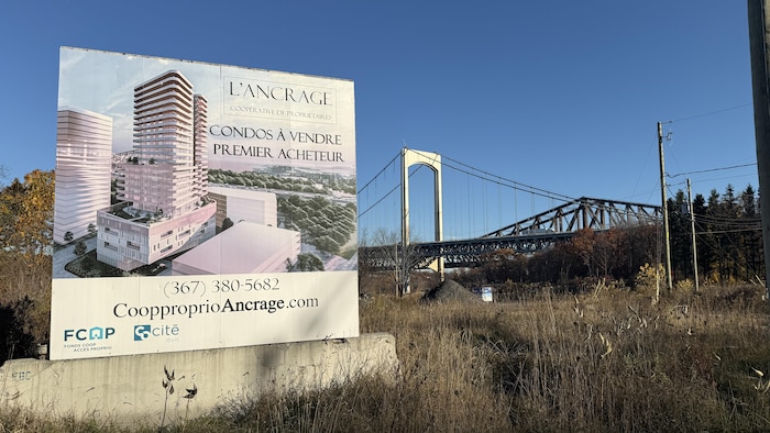 Une affiche indiquant « condos à vendre premier acheteur » tient debout sur un bloc de béton à proximité des ponts de Québec.