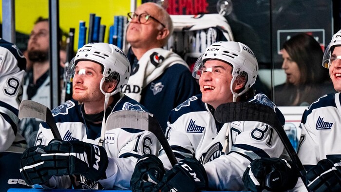 Des joueurs de hockey derrière une bande ont les yeux levés et sourient.