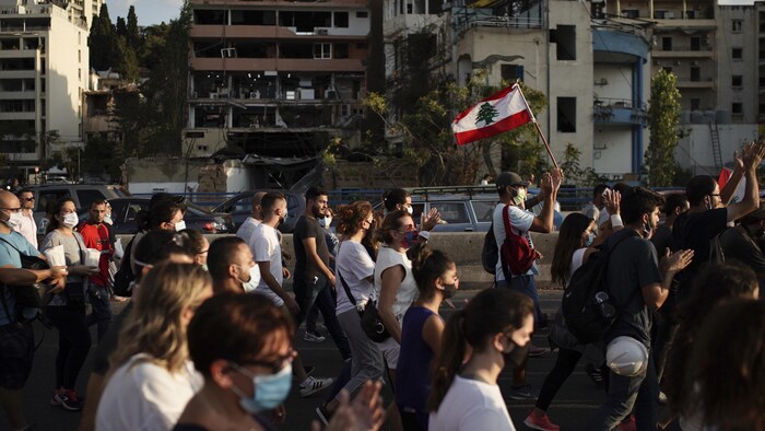 Des gens marchent devant des immeubles en ruines.