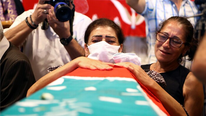 Une femme portant un masque pleure au-dessus d'un cercueil recouvert du drapeau libanais.