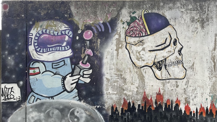 Une murale représentant un astronaute contrôlant avec une manette un cerveau qui plane au-dessus d'une ville en feu.