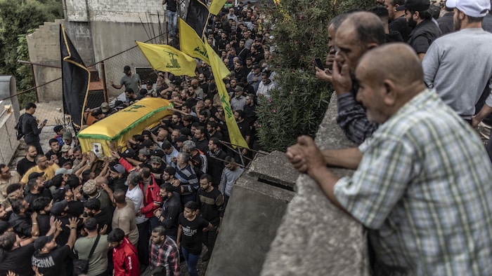 Une foule porte un cercueil drapé aux couleurs du Hezbollah.