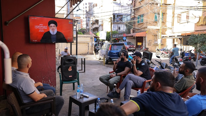 Dışarıda oturan erkekler Hasan Nasrallah'ın televizyonda yayınlanan konuşmasını dinliyor.