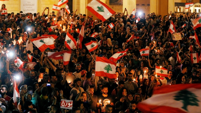 Une foule compacte brandissant des drapeaux du Liban dans une rue.