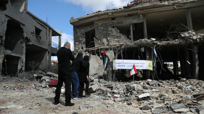 Trois personnes se tiennent debout devant les ruines d'un immeuble.