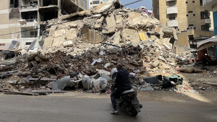 Un motard stationné devant un tas de ruines.