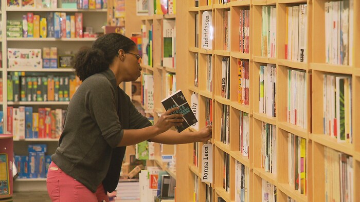 Une femme range des livres dans un rayon d'une librairie.