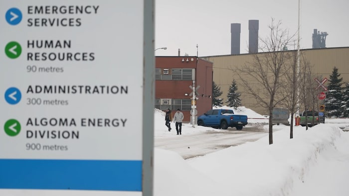Des travailleurs de l'aciérie Algoma Steel sortent de l'usine et marchent sur les routes enneigées, derrière une plaque.