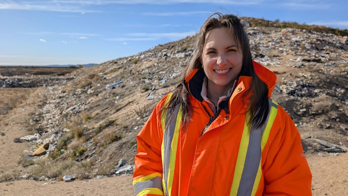 Mélissa Bernier porte une veste orange avec des bandes réfléchissantes. Elle se tient debout sur le lieu d'enfouissement.