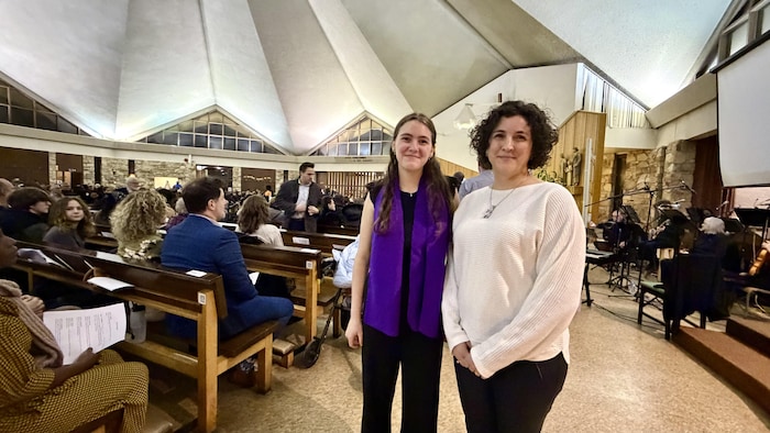 Lili Blanc et sa mère Marie-Claude Paradis sourient à la caméra, à l'intérieur d'une église où sont réunies plusieurs personnes. Un petit orchestre se trouve tout près. 