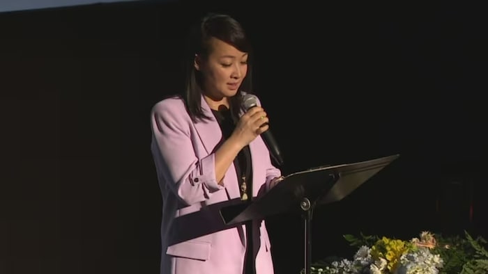 Lily Cheng est debout sur scène, un micro à la main.