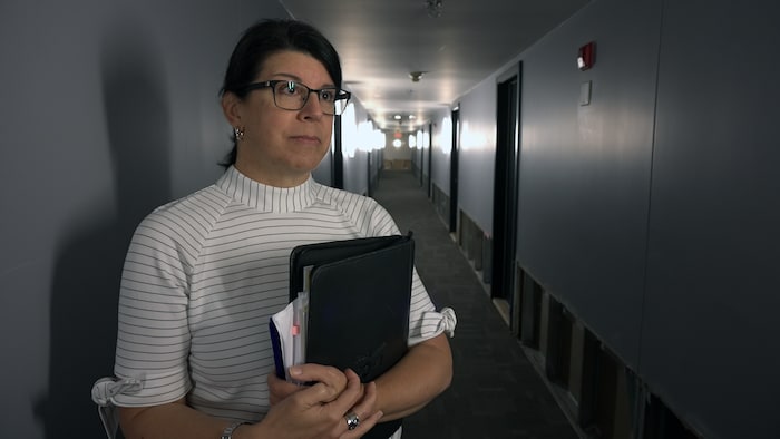 Une femme avec des lunettes dans un corridor qui tient un cartable.