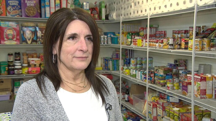 Une femme debout à côté et devant des étagères remplies de boîtes de conserve et de boîtes de céréales.