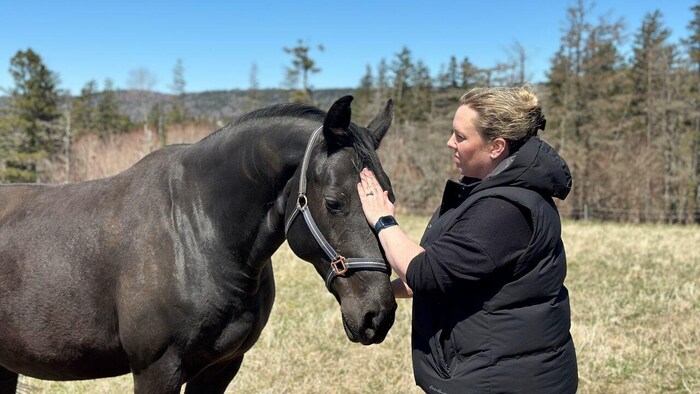 Une femme de profil caresse la tête d'un cheval noir.